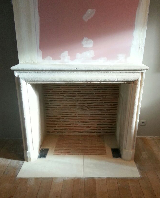 Une cheminée Louis XIV en pierre installée avec un intérieur réalisé en briquettes réfractaires.