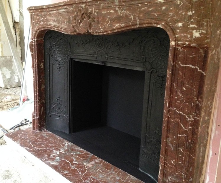 Une cheminée d'époque Louis XV en marbre avec son intérieur en fonte